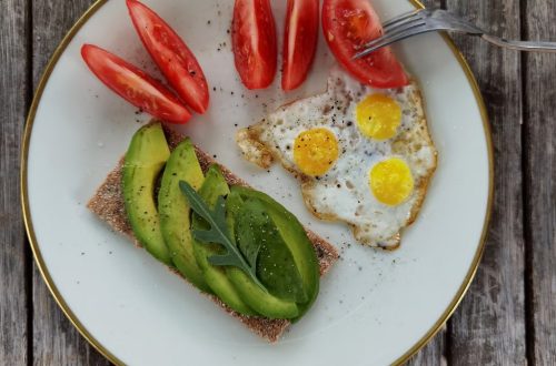 Delicious breakfast plate with sliced avocado, tomatoes, and sunny-side-up quail eggs.