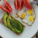 Delicious breakfast plate with sliced avocado, tomatoes, and sunny-side-up quail eggs.