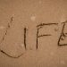 The word 'Life' artistically drawn in sand, symbolizing change and nature's impermanence.